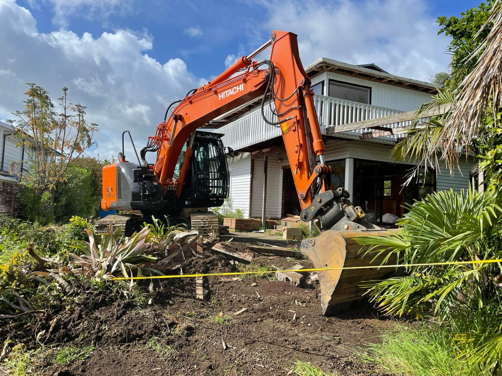 Excavator clearing trees beside a house